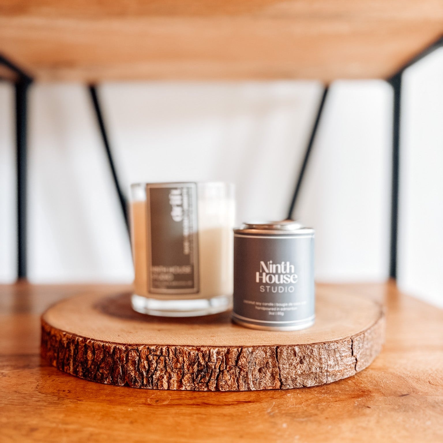 Candle and tin labeled 'Ninth House Studio' on a wooden surface