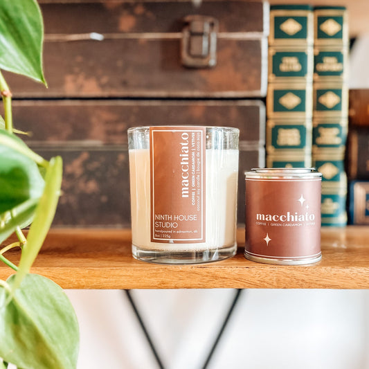 Two Ninth House Studio candles labeled 'macchiato' on a wooden surface with a blurred background