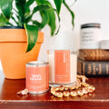 Candle and tin with 'Ninth House Studio' branding on a wooden surface with a plant in the background.