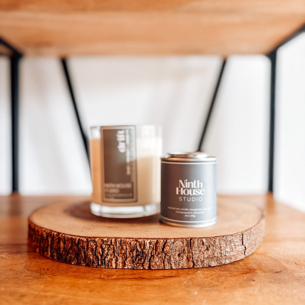 Candle and tin labeled 'Ninth House Studio' on a wooden surface